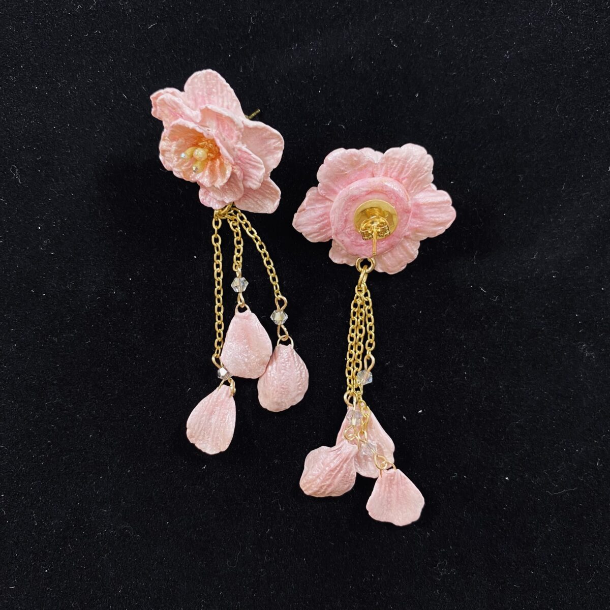 Pink blossom earrings made out of polymer clay with three gold chains ending in clay petals.