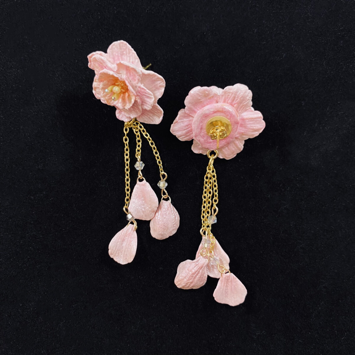 Pink blossom earrings made out of polymer clay with three gold chains ending in clay petals.