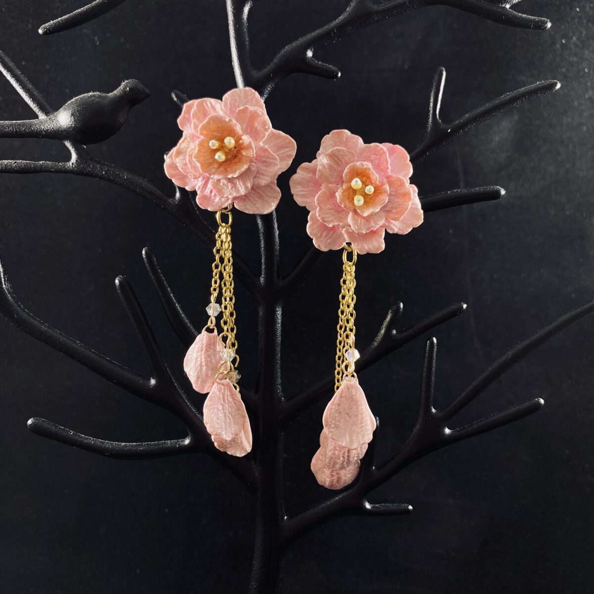 Pink blossom earrings made out of polymer clay with three gold chains ending in clay petals.