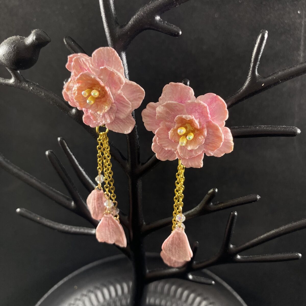Pink blossom earrings made out of polymer clay with three gold chains ending in clay petals.