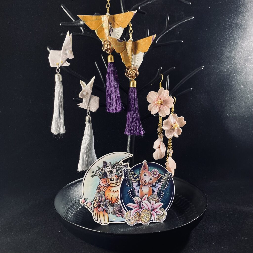 Handmade earrings and stickers on a stand.